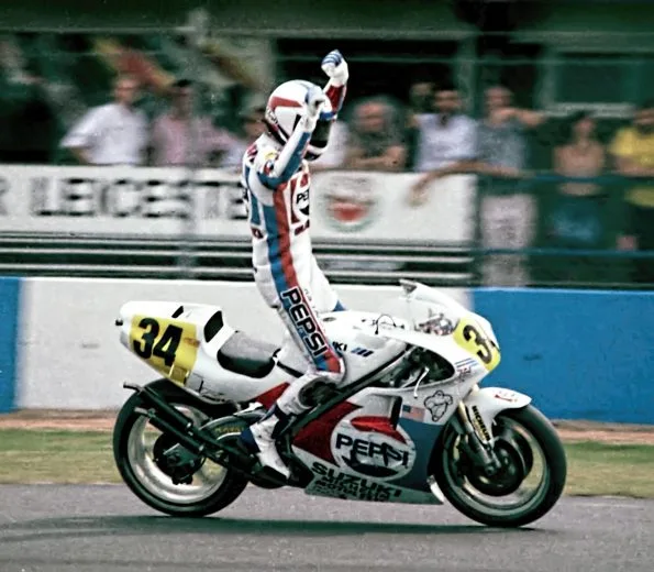 Kevin Schwantz, sitting on his Pepsi Cola Suzuki, waving his hands in the air and celebrating after winning the 1989 British Grand Prix.