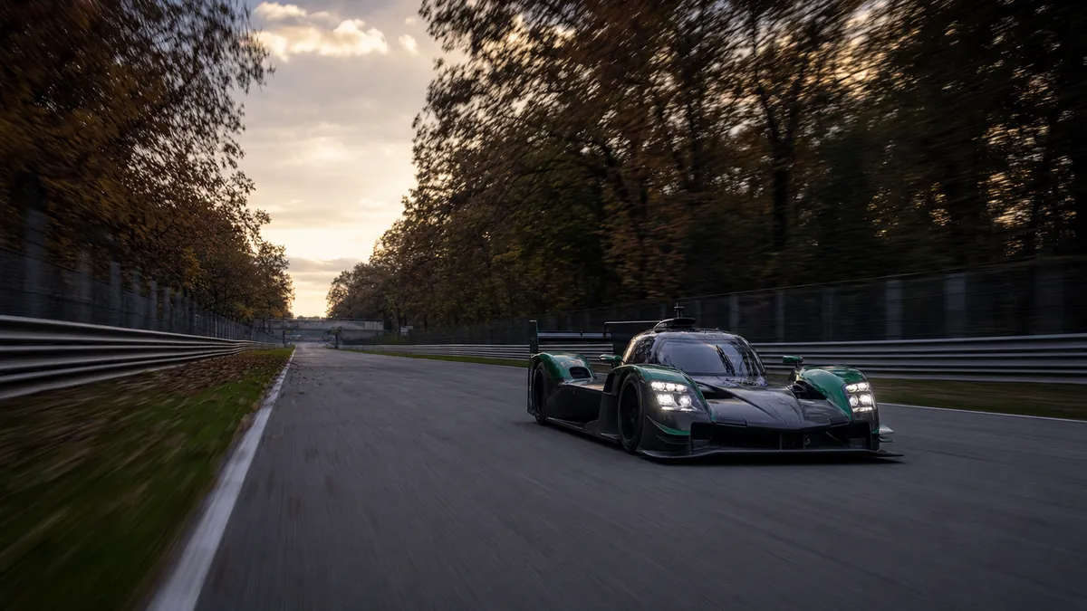 Fictional green endurance prototype racing along a tree-lined Italian circuit at dusk