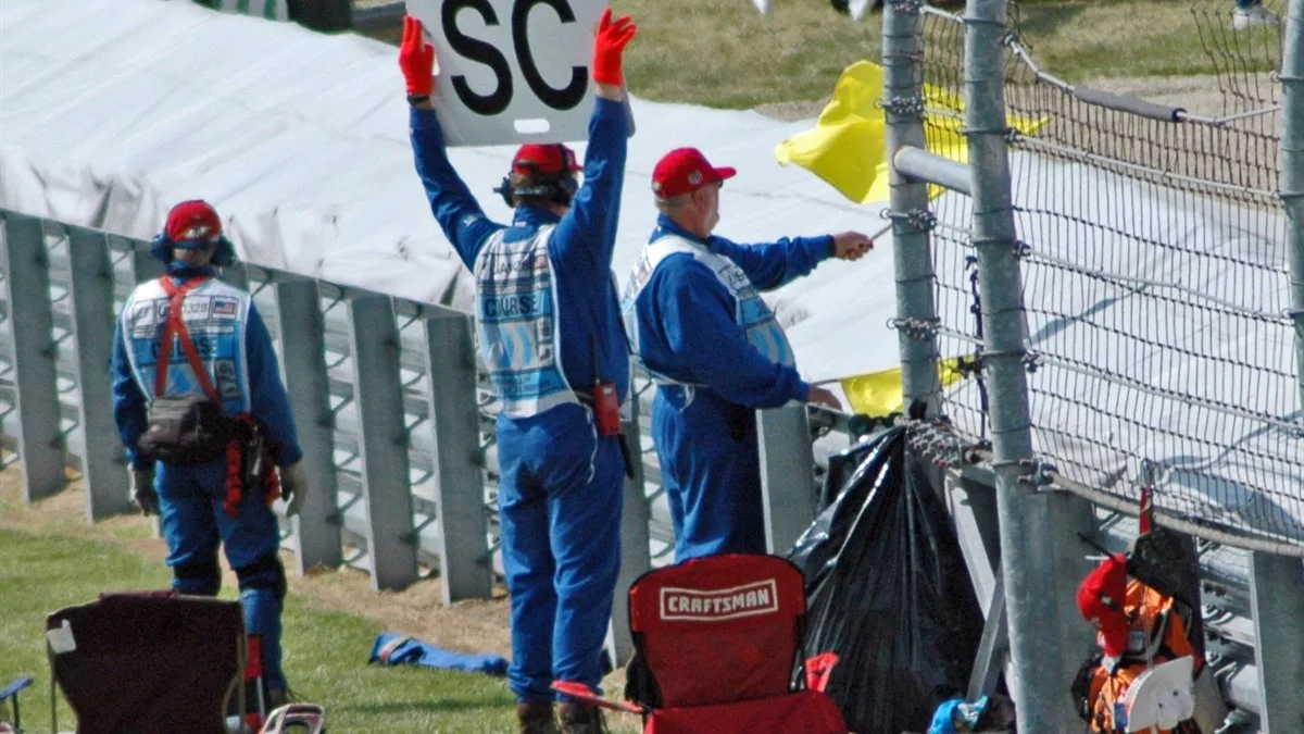 Formula 1 marshals displaying yellow flags and a Safety Car sign beside the circuit