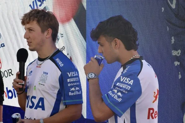 Liam Lawson talking on stage with a Racing Bulls teammate at a fan zone event in team gear.
