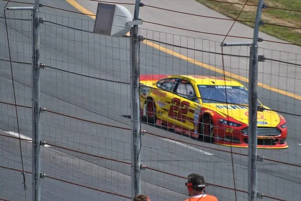 Joey Logano driving the red and yellow number 22 Team Penske Shell Ford Fusion on track in 2015.
