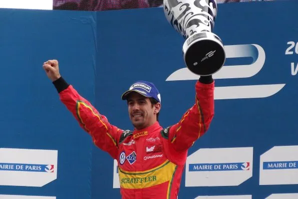 Lucas di Grassi on the podium in his red and yellow ABT Schaeffler overalls, one arm raised and the winner's trophy held aloft, after the 2016 Paris ePrix.