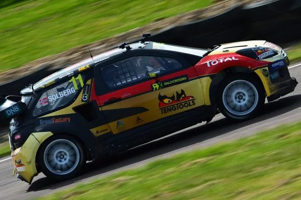 Petter Solberg’s number 11 PSRX Citroën DS3 rallycross Supercar in yellow, red and black at speed at Lydden Hill in 2014, shot side-on with the background blurred