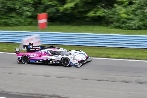 The pink, white and blue Meyer Shank Racing Acura ARX-06, number 60, cornering at Watkins Glen during the 2023 six-hour race, panned against blue barriers.