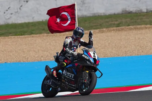 Razgatlıoğlu standing on his BMW M1000RR holding a Turkish flag aloft on a lap of honour at the 2025 French round of the Superbike World Championship